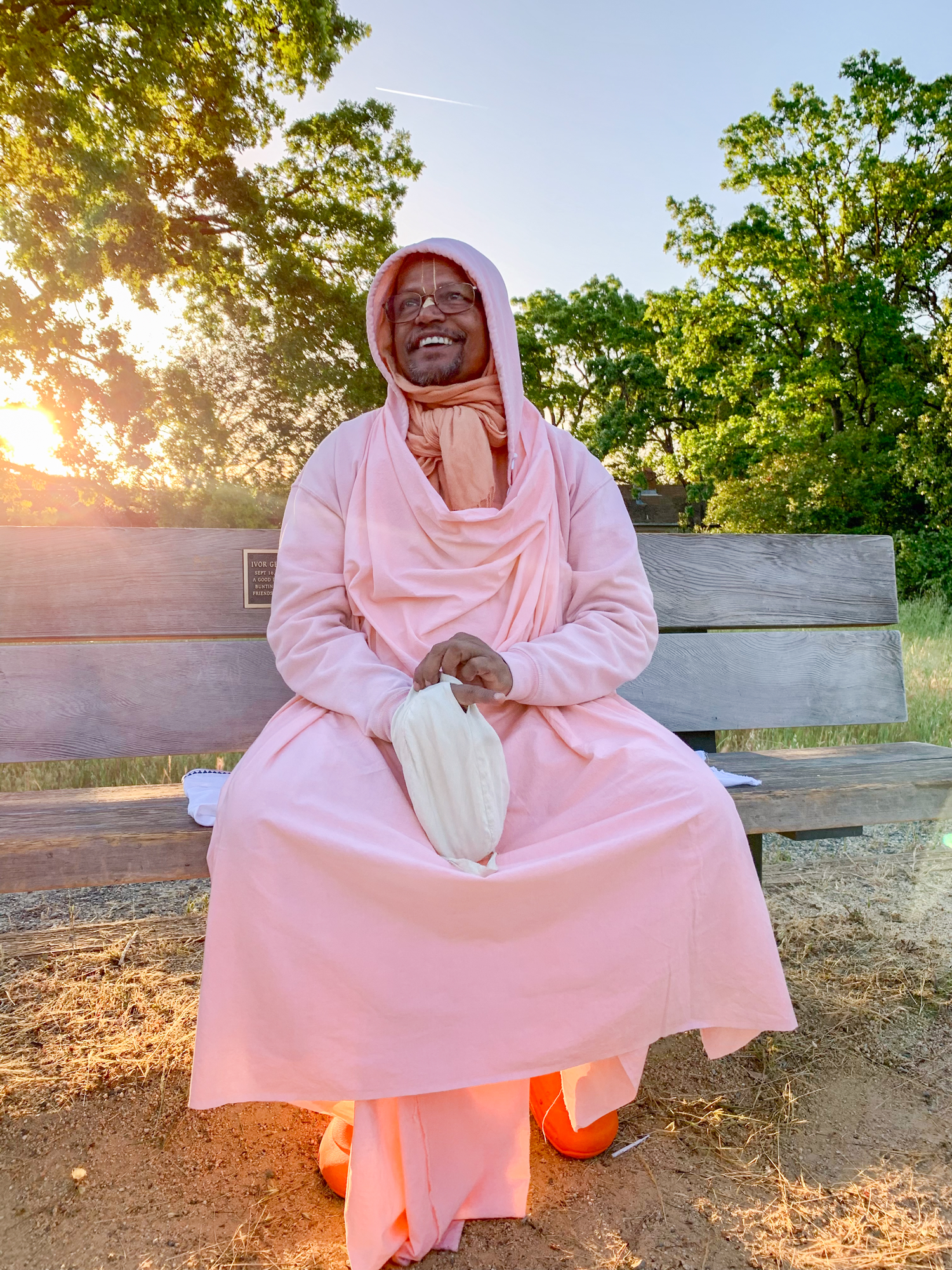 Srila Bhakti Swarup Sridhara Maharaja sitting on a bench backlit by the sun while chanting papa
